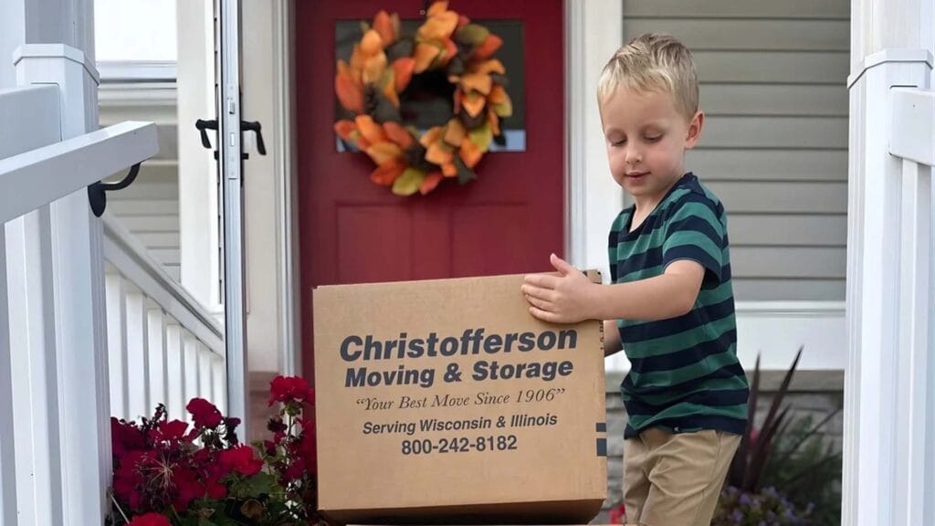 Young child picking up a Christofferson moving box in front of a residential porch