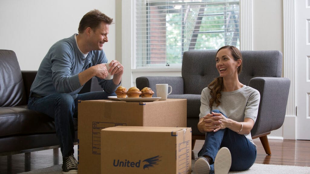 Couple eating muffins in the living room and using boxes as tables