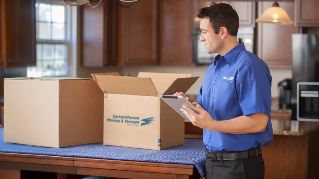 Christofferson employee in a kitchen review moving documents on tablet, with boxes on the dinning table.